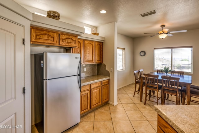 kitchen featuring tasteful backsplash, a healthy amount of sunlight, light tile patterned floors, and stainless steel refrigerator