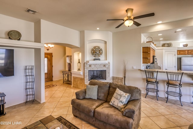 living room featuring light tile patterned flooring, ceiling fan with notable chandelier, and a tile fireplace