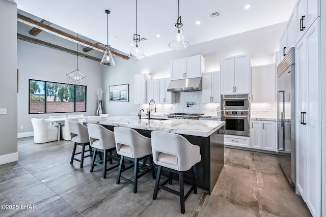 816 Isola Bella Loop, Lake Havasu City, AZ 86403 - kitchen with under cabinet range hood, decorative backsplash, stainless steel built in fridge, a center island with sink, and light stone countertops