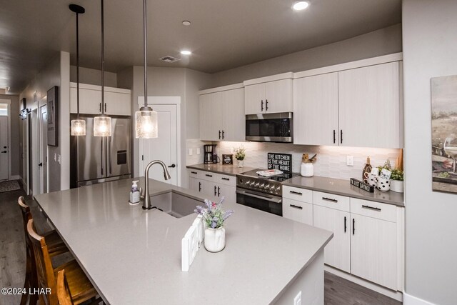 kitchen featuring sink, tasteful backsplash, hanging light fixtures, a center island with sink, and stainless steel appliances