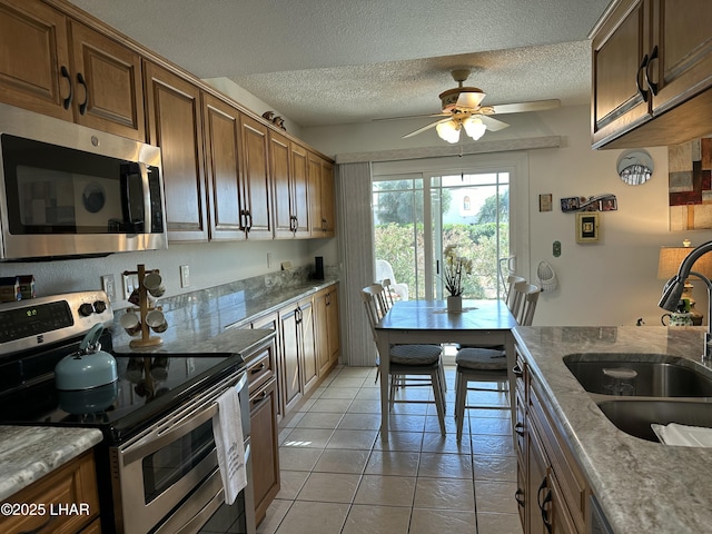 kitchen featuring sink, ceiling fan, light tile patterned floors, a textured ceiling, and appliances with stainless steel finishes