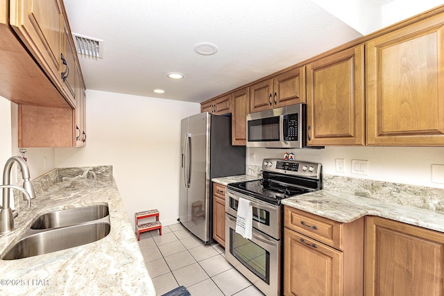 kitchen with stainless steel appliances, light stone counters, brown cabinetry, and a sink