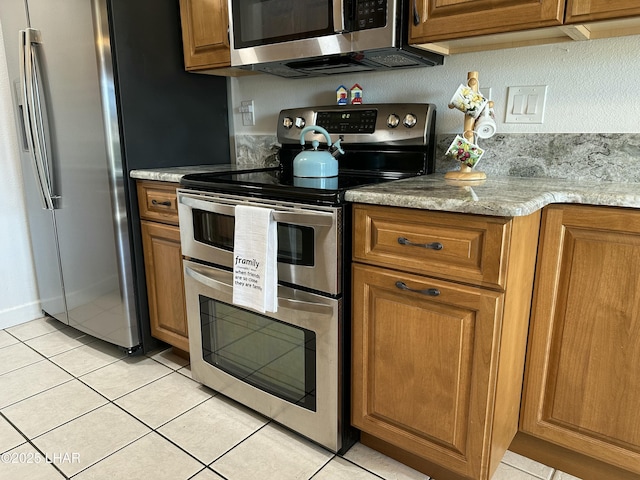 kitchen with appliances with stainless steel finishes, light stone counters, and light tile patterned floors