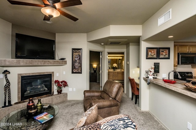 living room with ceiling fan, light colored carpet, a tiled fireplace, and sink