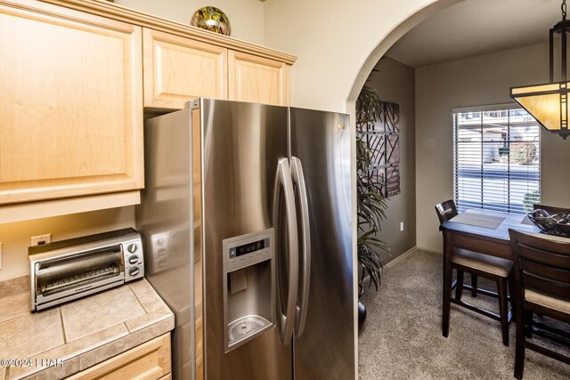 kitchen with dark colored carpet, decorative light fixtures, stainless steel fridge with ice dispenser, light brown cabinets, and tile counters