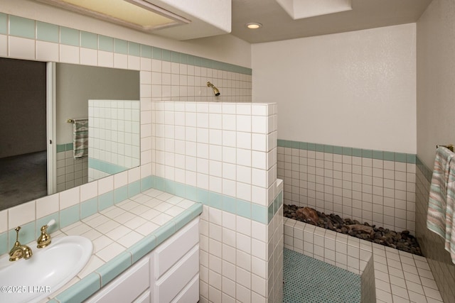 bathroom featuring walk in shower, vanity, and tile walls