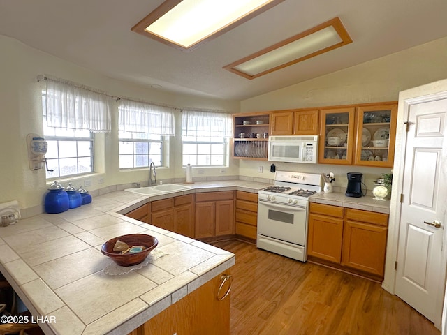 kitchen featuring white appliances, brown cabinetry, tile countertops, lofted ceiling, and a sink