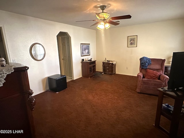 sitting room with arched walkways, dark carpet, baseboards, and ceiling fan