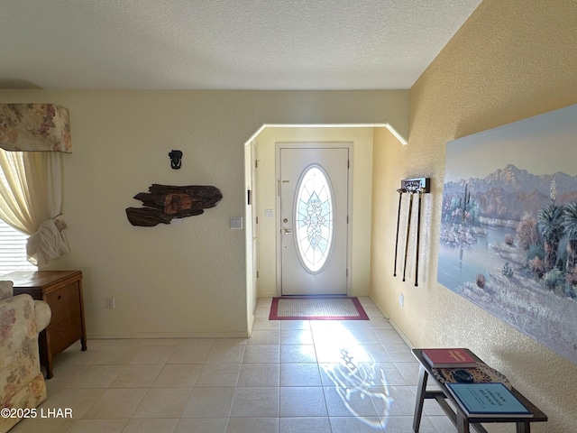 entrance foyer with light tile patterned flooring, a textured wall, and a textured ceiling