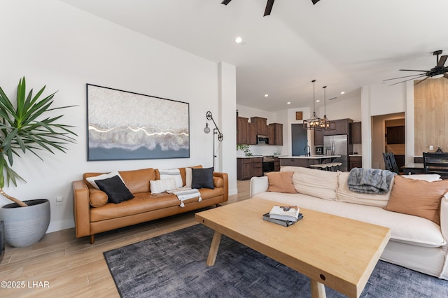 living room with ceiling fan with notable chandelier, light hardwood / wood-style flooring, and vaulted ceiling