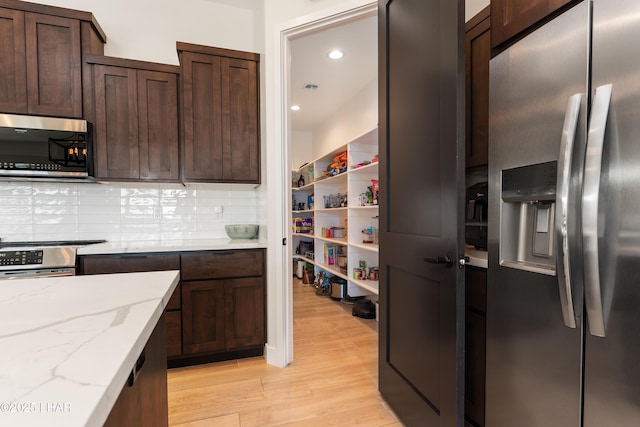 kitchen with dark brown cabinetry, light stone counters, appliances with stainless steel finishes, light hardwood / wood-style floors, and backsplash