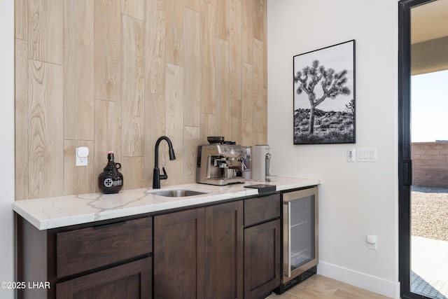 bar featuring wine cooler, sink, light stone counters, light hardwood / wood-style flooring, and dark brown cabinets