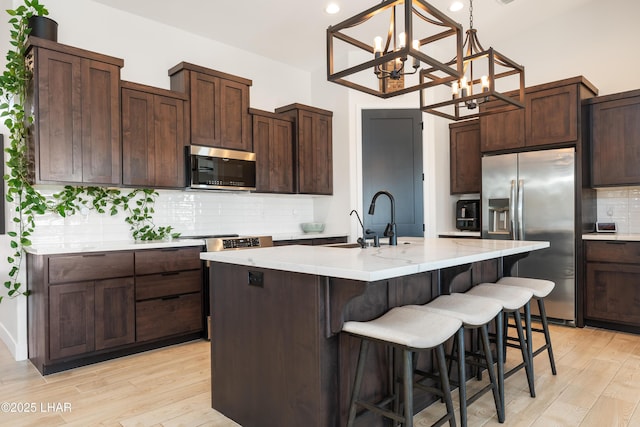 kitchen featuring dark brown cabinetry, appliances with stainless steel finishes, light hardwood / wood-style floors, and an island with sink