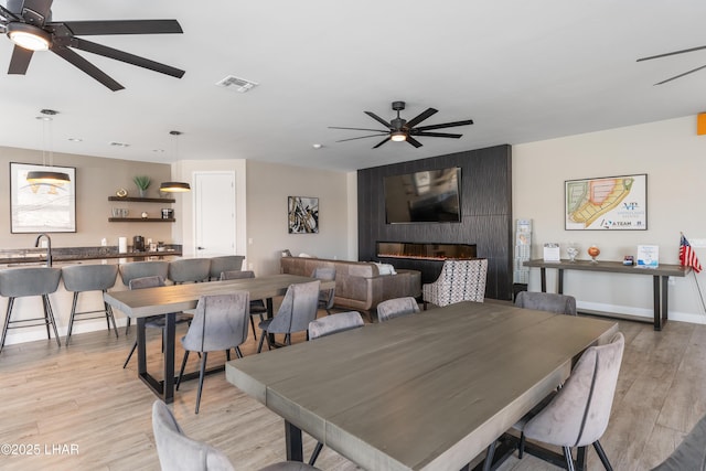 dining space with ceiling fan, a fireplace, and light hardwood / wood-style floors