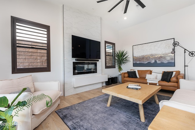 living room with a premium fireplace, wood-type flooring, and ceiling fan