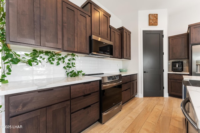 kitchen featuring appliances with stainless steel finishes, backsplash, light stone countertops, dark brown cabinets, and light wood-type flooring