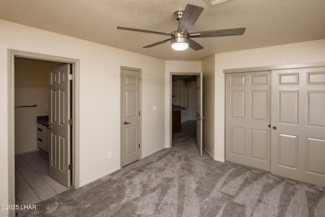 unfurnished bedroom featuring ensuite bathroom, a textured ceiling, a closet, carpet, and ceiling fan