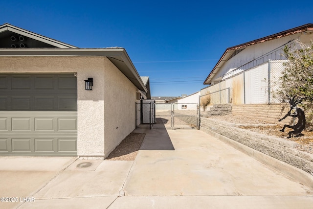 view of side of property with stucco siding, fence, a garage, and a gate