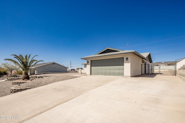 view of property exterior featuring an attached garage, fence, stucco siding, driveway, and a gate