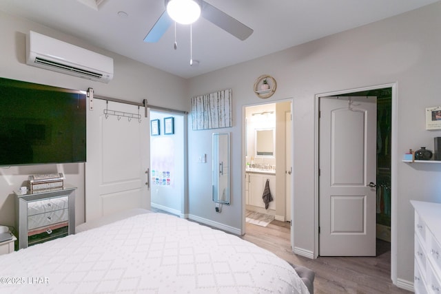 bedroom featuring an AC wall unit, connected bathroom, a barn door, ceiling fan, and wood finished floors