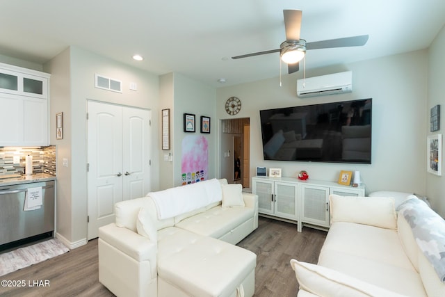 living area featuring wood finished floors, an AC wall unit, ceiling fan, and visible vents