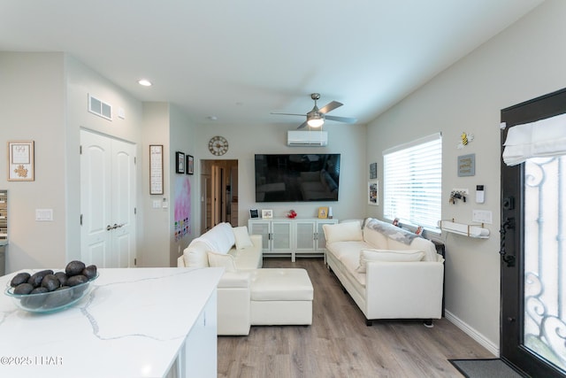 living room featuring visible vents, baseboards, wood finished floors, a ceiling fan, and an AC wall unit