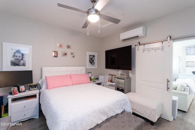 bedroom featuring a barn door, ceiling fan, wood finished floors, and a wall unit AC
