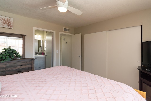 bedroom with a textured ceiling, a ceiling fan, ensuite bathroom, visible vents, and a closet