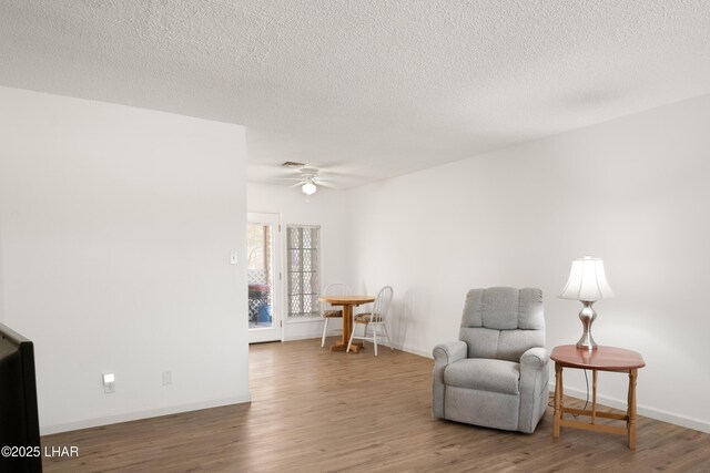 living area featuring ceiling fan, a textured ceiling, visible vents, wood finished floors, and baseboards
