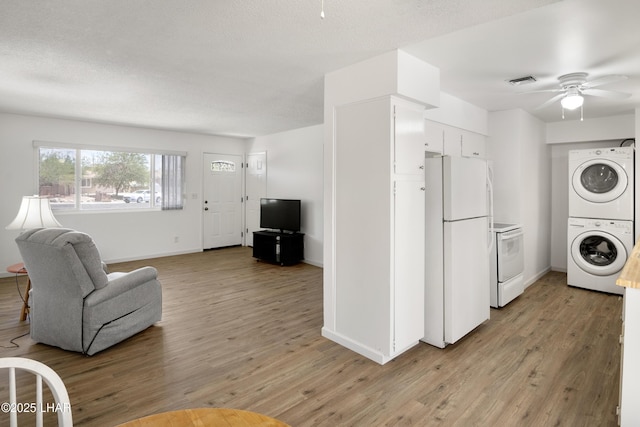 living area featuring ceiling fan, stacked washing maching and dryer, baseboards, and light wood-style floors