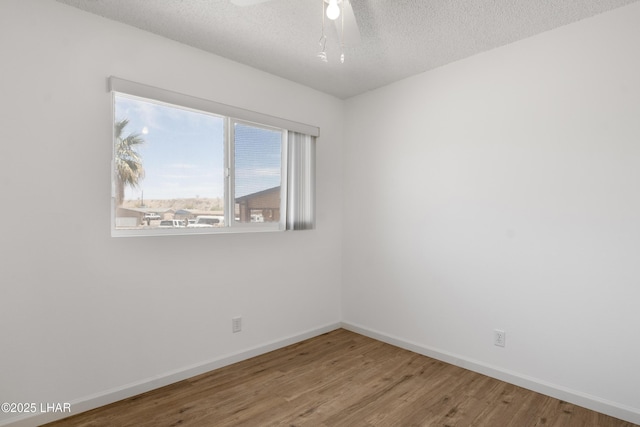 empty room featuring a textured ceiling, baseboards, ceiling fan, and wood finished floors