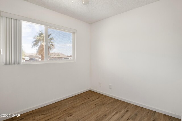 spare room featuring baseboards, a textured ceiling, and wood finished floors