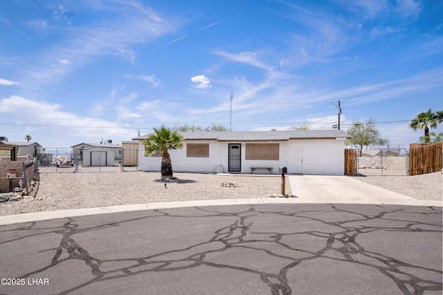 ranch-style house with a storage unit, fence, stucco siding, and concrete driveway