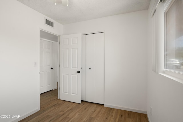 unfurnished bedroom with a textured ceiling, visible vents, wood finished floors, baseboards, and a closet