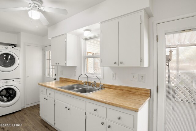 clothes washing area featuring laundry area, wood finished floors, stacked washing maching and dryer, ceiling fan, and a sink