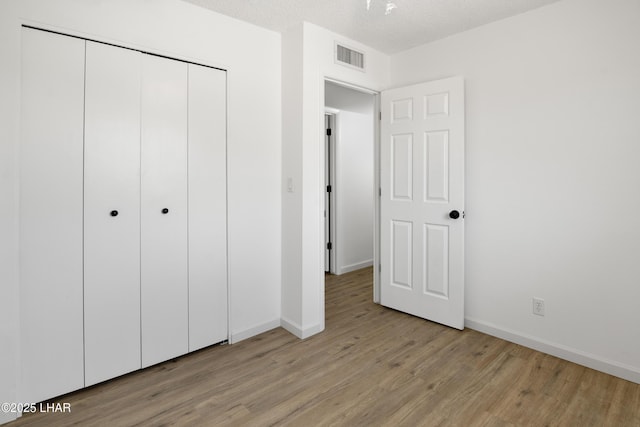 unfurnished bedroom featuring baseboards, visible vents, light wood finished floors, and a closet