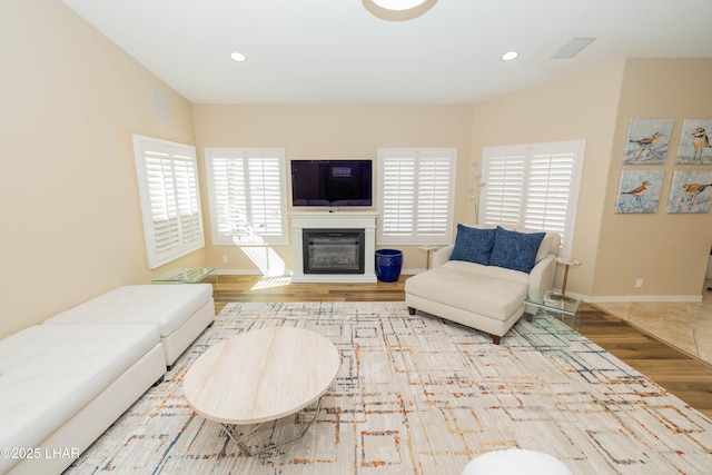 living room with baseboards, wood finished floors, a glass covered fireplace, and recessed lighting