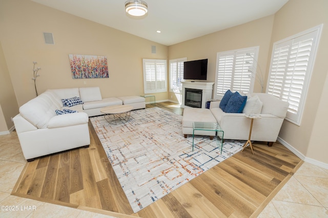 tiled living area with visible vents, baseboards, a glass covered fireplace, vaulted ceiling, and recessed lighting