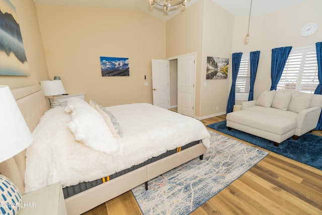 bedroom with high vaulted ceiling, a chandelier, baseboards, and wood finished floors