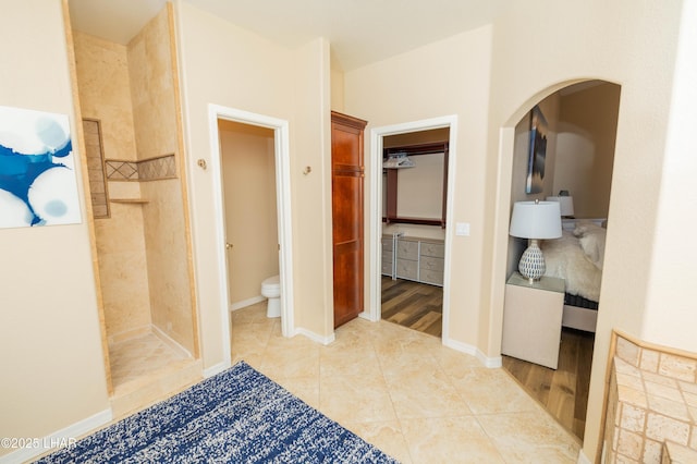 full bathroom with baseboards, toilet, tile patterned floors, a spacious closet, and a tile shower