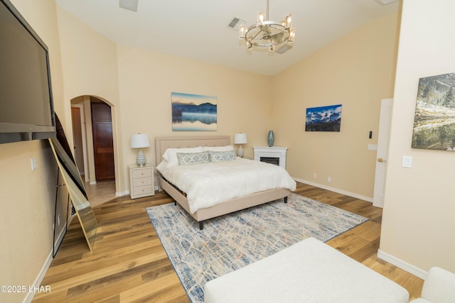 bedroom with arched walkways, light wood finished floors, visible vents, and a notable chandelier