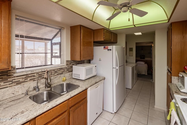 kitchen with brown cabinets, a sink, light tile patterned floors, washer / dryer, and white appliances