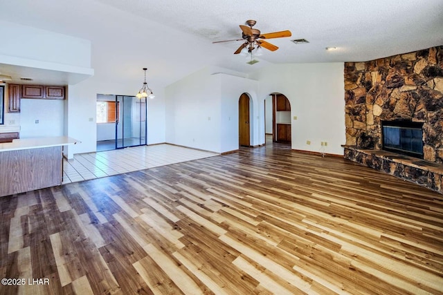 unfurnished living room featuring vaulted ceiling, a stone fireplace, ceiling fan, a textured ceiling, and light hardwood / wood-style flooring