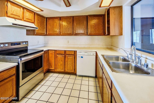 kitchen featuring dishwasher, sink, stainless steel range with electric cooktop, light tile patterned floors, and a tray ceiling