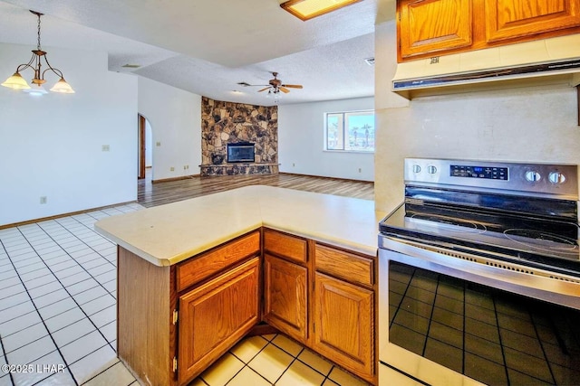 kitchen with light tile patterned floors, electric range, a fireplace, decorative light fixtures, and kitchen peninsula