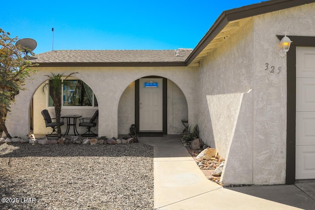 doorway to property with a shingled roof and stucco siding