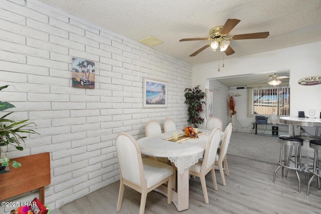 dining room with light hardwood / wood-style floors, a textured ceiling, and brick wall