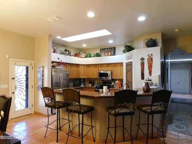 kitchen with appliances with stainless steel finishes, a breakfast bar, a skylight, backsplash, and light tile patterned floors