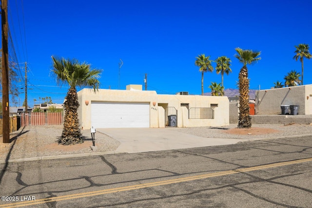 pueblo-style home featuring stucco siding, a gate, a fenced front yard, concrete driveway, and an attached garage