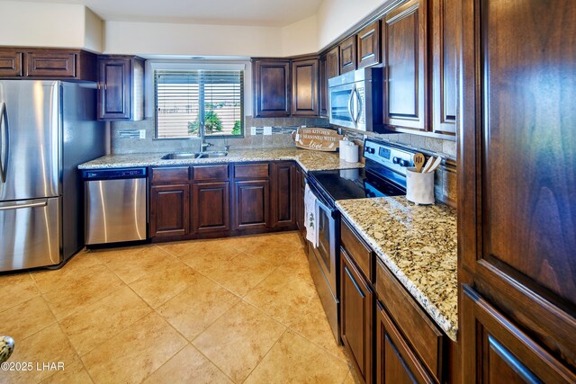 kitchen featuring light stone counters, light tile patterned floors, backsplash, appliances with stainless steel finishes, and a sink